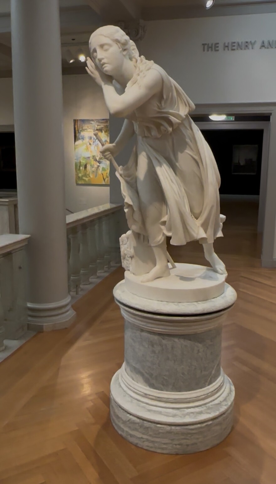 A marble statue of a woman cupping her ear sits on a pedestal.