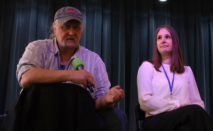 Two people sit on a stage.