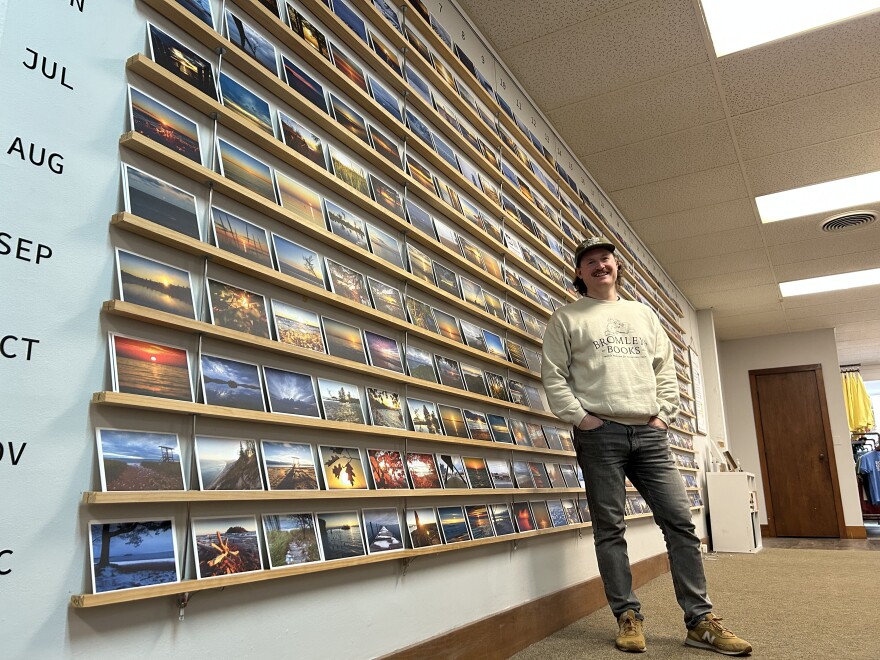 Bugsy Sailor standing in front of The Sunrise Gallery. It's a wall of 365 photos located in Upper Peninsula Supply Company – a retail shop he runs in downtown Marquette. (credit: Dan Wanschura / Points North)