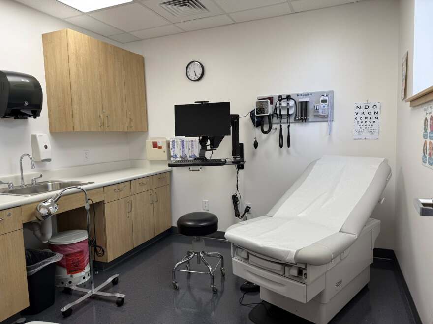 A clean, white medical exam room, with an exam table, stool, computer, sink, and various other medical equipment.