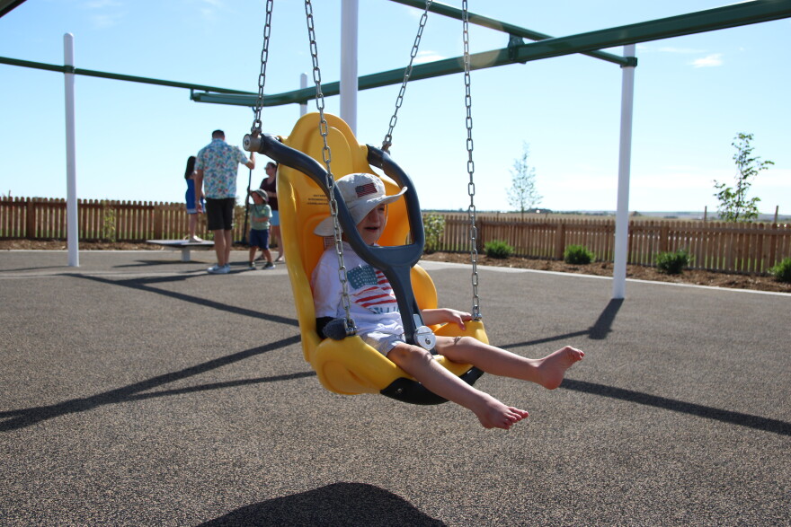 A young boy in a bucket hat with an American flag on it and a white shirt with an American flag on it sits in a large yellow plastic chair hanging from a set of chains. His feet are dangling from the chair. 