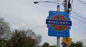 Blue street sign that says Roselawn with red roses.