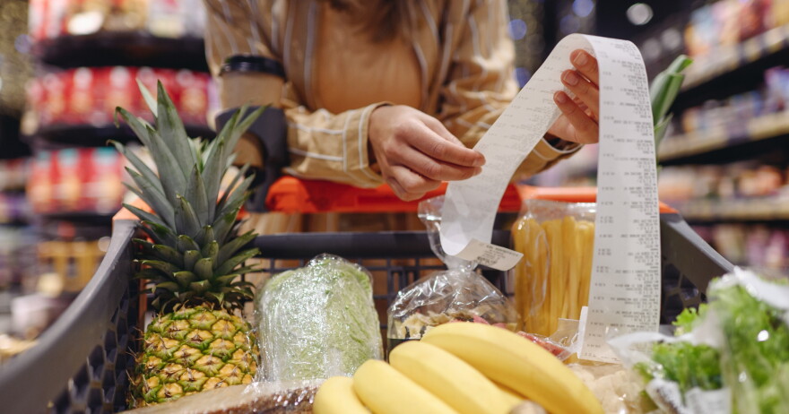 A person reads a receipt held over a cart of groceries.
