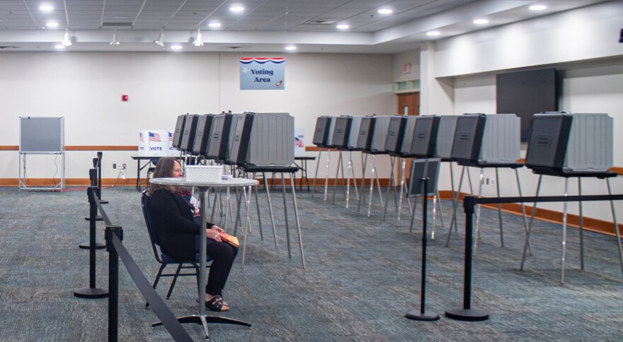 About a dozen voting machines set up in a large conference room. One poll worker sits to greet voters.