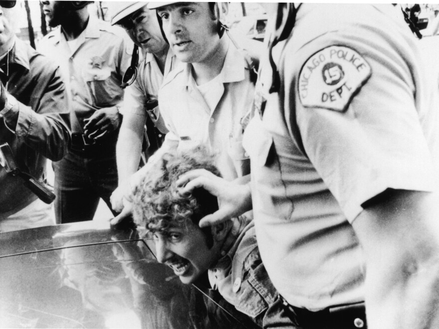Officers from the Chicago Police Department push a protester's head against the hood of a car after he climbed onto a wooden barricade near the Democratic National Convention and waved a Viet Cong flag during anti-Vietnam War demonstrations in 1968.