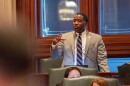 Man in a suit speaking into a microphone in a legislative chamber