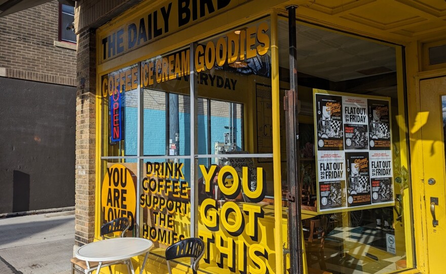 The exterior of a coffee shop is painted yellow with supportive messages on the large windows in front.