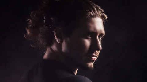 A man with a goatee and hair in a bun is staring off into the distance