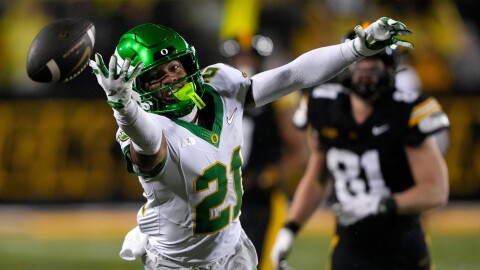 An Oregon football player reaches for a football that is just out of his reach
