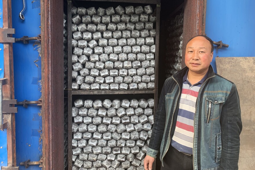 Sun Dahui stands outside a self-made oven, which heats logs of mushroom-growing medium before they are put into greenhouses to germinate. The cooperative hopes to expand into making mushroom-based sauces soon.