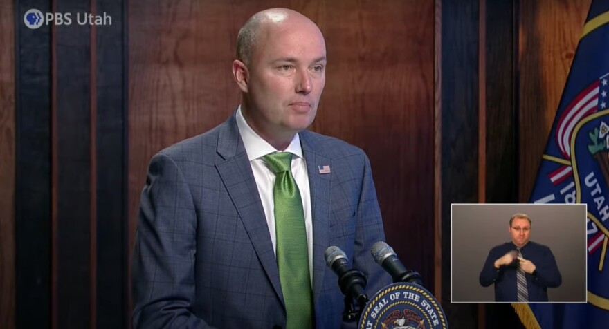 Governor Cox standing behind a podium at a monthly news conference. 