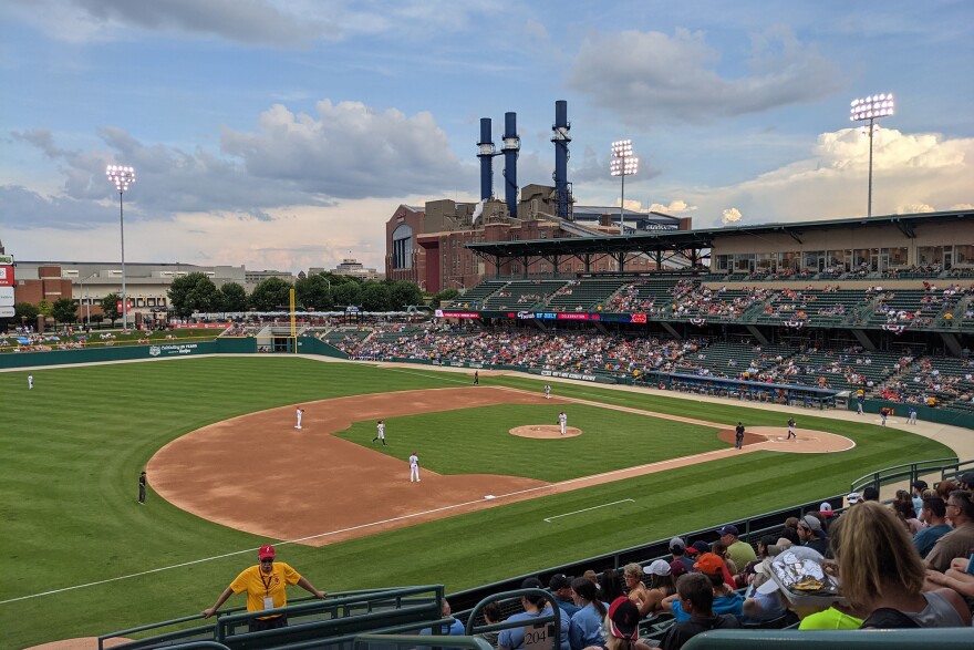 A picture of a game in the Indianapolis Indians Victory Field, taken from the stands at a middle distance. A baseball diamond, a few players and a crowd nearly filling up the seats across the field can be seen.