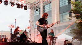 A woman in black playing electric guitar on an outdoor stage