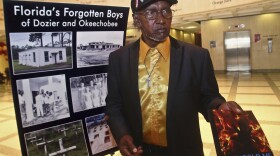 Johnny Lee Geddy, a "White House Boy" at the Arthur G. Dozier School for Boys in Jackson County from 1957-61, shows reporters a book he wrote about the experience Tuesday April 4, 2017, in the Capitol in Tallahassee, Fla. Geddy had just attended a Senate Judiciary Committee meeting where a proposal to formally apologize for the abuse that happened at the school was discussed. The proposal was passed that year. (AP Photo/Phil Sears)