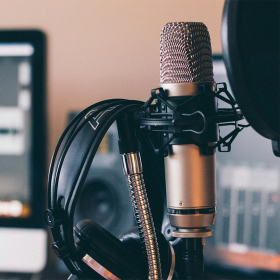 A grey microphone with headphones hung on it in front of a blurry background.