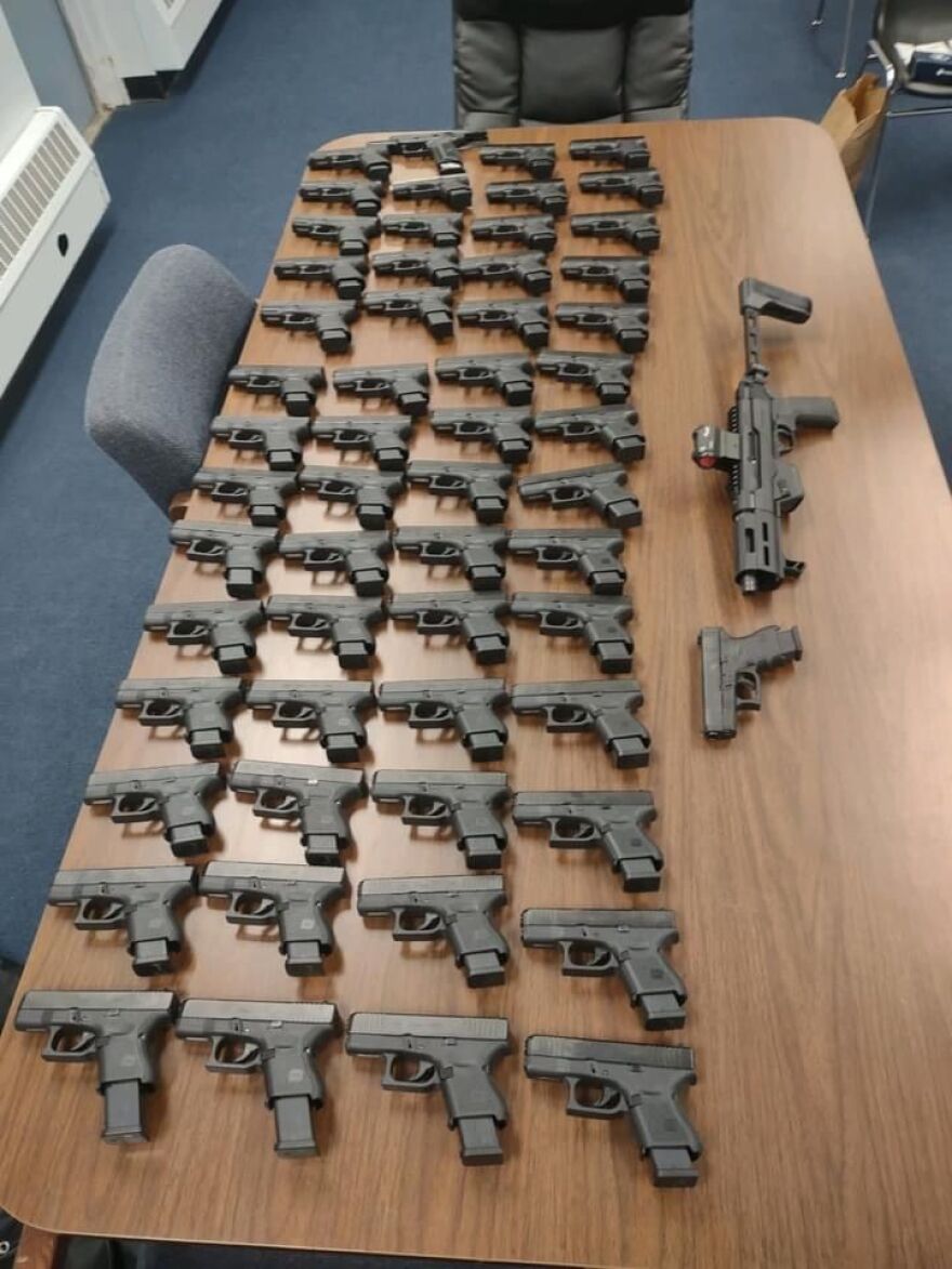 Police in Mt. Morris display 58 guns that a Canadian man is accused of illegally possessing when he was stopped for traffic violations in that village.