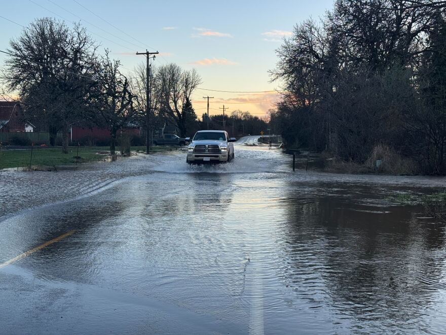 A pick up truck drives through water covering a two-lane road.