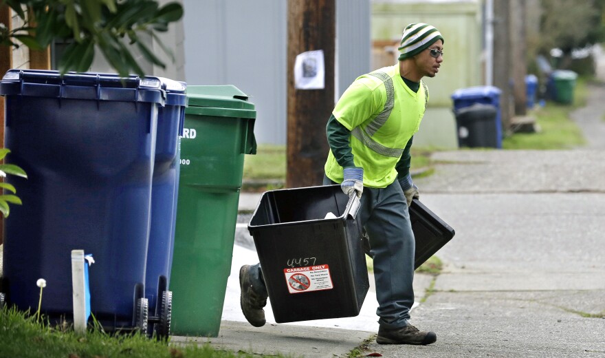 In this photo taken Monday, Dec. 22, 2014, garbage collector Anousone Sadettanh runs to his truck with a small residential garbage bin as larger yard waste and recycling bins stand behind as he works his pickup route in Seattle. Fail to recycle in Seattle and you can get a ticket from the garbage collector. The city says it will start enforcing new recycling requirements on Jan. 1 with warning tags. Careless residents will start seeing fines July 1 on their bills  $1 per violation, $50 for a commercial or apartment building.