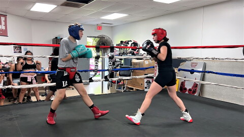  Two young boxers face off in a ring. They wear t-shirts, shorts, boxing gloves and protective head gear.