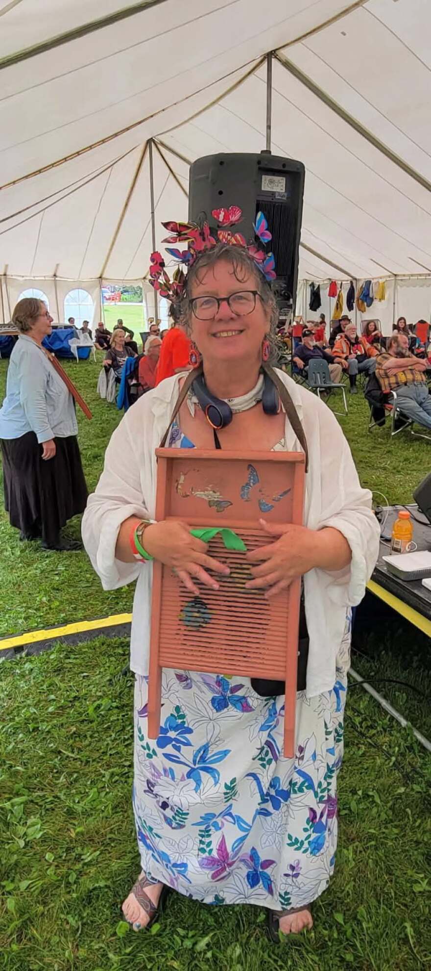 A woman in a white floral dress and colorful butterflies in her hair holds a washboard