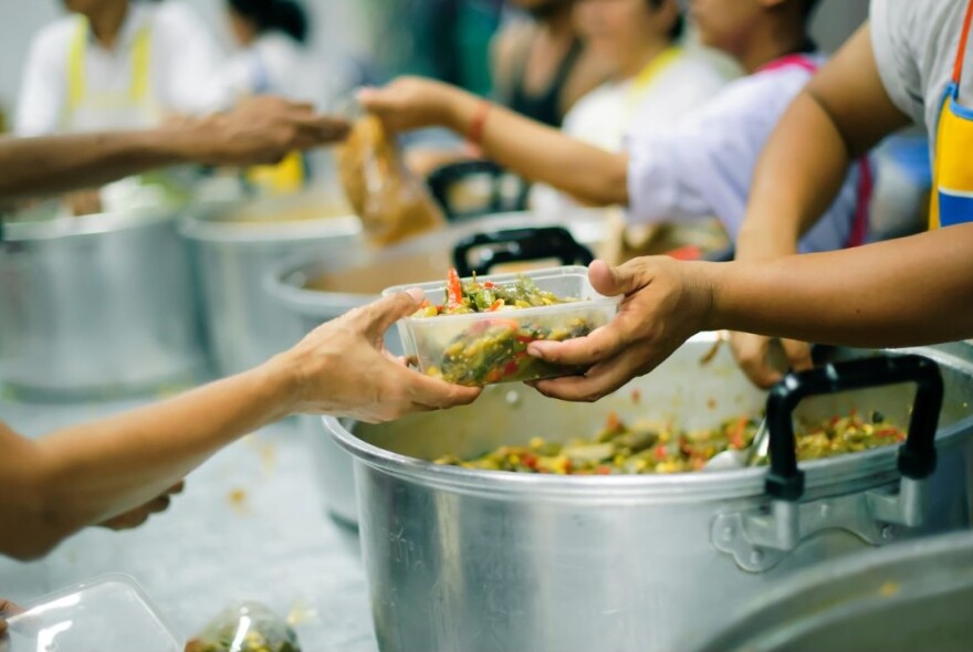 Large pots of mixed food, and hands passing a container with food in it to others' hands