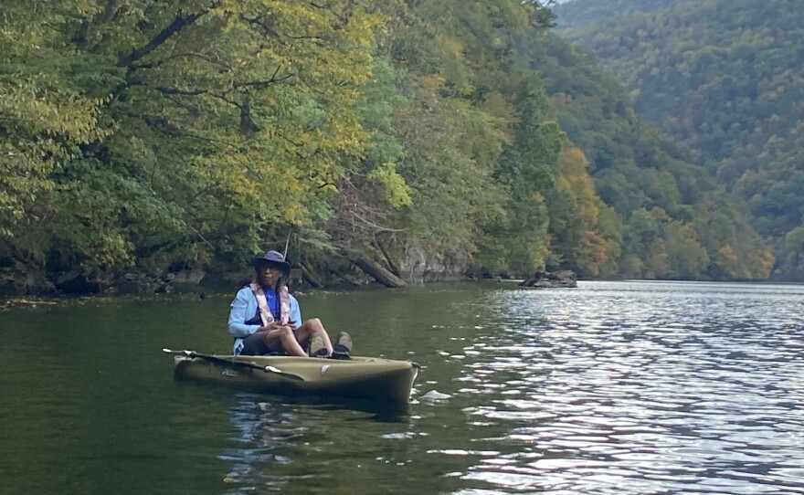 Henry Nelson sitting in kayak on a body of water with trees and mountains in the background