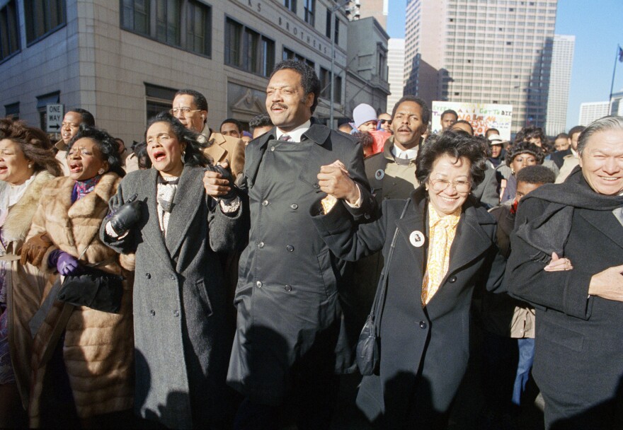 FILE - Coretta Scott King holds hands while singing with the Rev. Jesse Jackson and Christine Farris, the sister of Dr. Martin Luther King, Jr., as they parade on Peachtree Street in Atlanta on Monday, Jan. 19, 1987 to honor King's birthday. At left in Mrs. Alveda king Beall and at right is Lupita Aquino Kashiwahara. (AP Photo/Charles Kelly, File)
