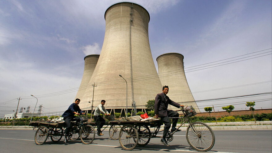Workers ride past cooling towers at a coal-fired power plant on the outskirts of Beijing. Such power plants are at the center of a debate about the future of energy production in China and the U.S.