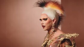 A drag queen looking left with a gold and black mohawks and gold outfit