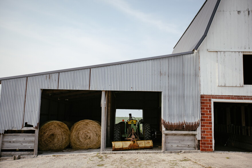 A barn roof covers a tractor and hay bales.