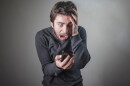 Man looks horrified as he receives a robocall on his cell phone.