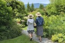 Two women in sundresses walk through a manicured landscape with a mountain view in the background.