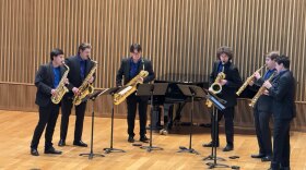 A saxophone sextet is performing on stage, pictured from behind the heads of the audience