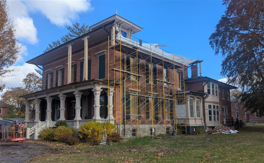 A large brick building has white columns in the front and is surrounded by a scaffolding on one side.