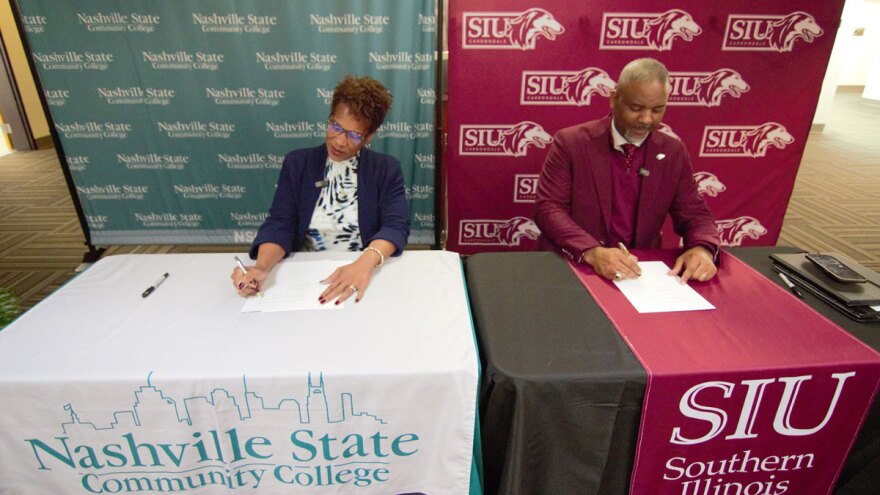 School leaders sit at a table signing papers.