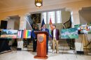 An African American man speaks at a podium with two people behind him and 4 posters of street murals. 