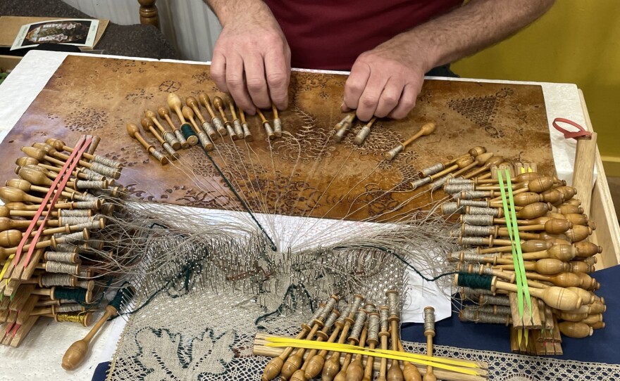 A man is making lace using many bobbins.