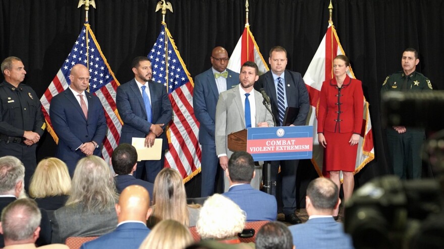 Florida Attorney General James Uthmeier is flanked by law enforcement and other leaders as he stands behind a podium that has a sign with the words "Combat violent extremism."