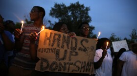Demonstrators hold candles and signs Thursday in Ferguson, Mo. Hundreds of people protesting the death of Michael Brown marched through the streets of Ferguson alongside state troopers on Thursday.