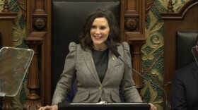 Governor Gretchen Whitmer staying behind a podium smiling. 