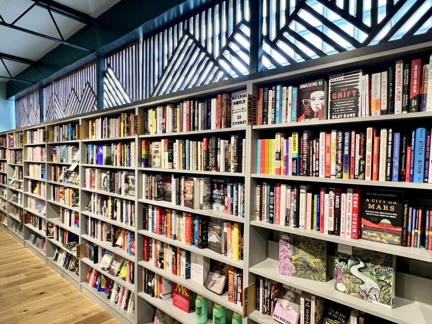 Books stacked on columns of gray bookshelves on a wall. Above the bookshelves are decorative panels cut in a diagonal and vertical pattern.