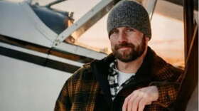 A man in a gray beanie looks into the camera while standing in front of a closely cropped small airplane.