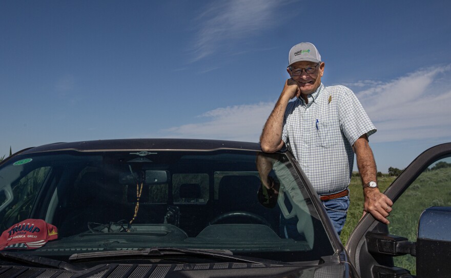 Rod Lenz stands inside the door well of the drivers side of his truck with the car door open. A read Trump "Make America Great Again" hat sits on the dash. the