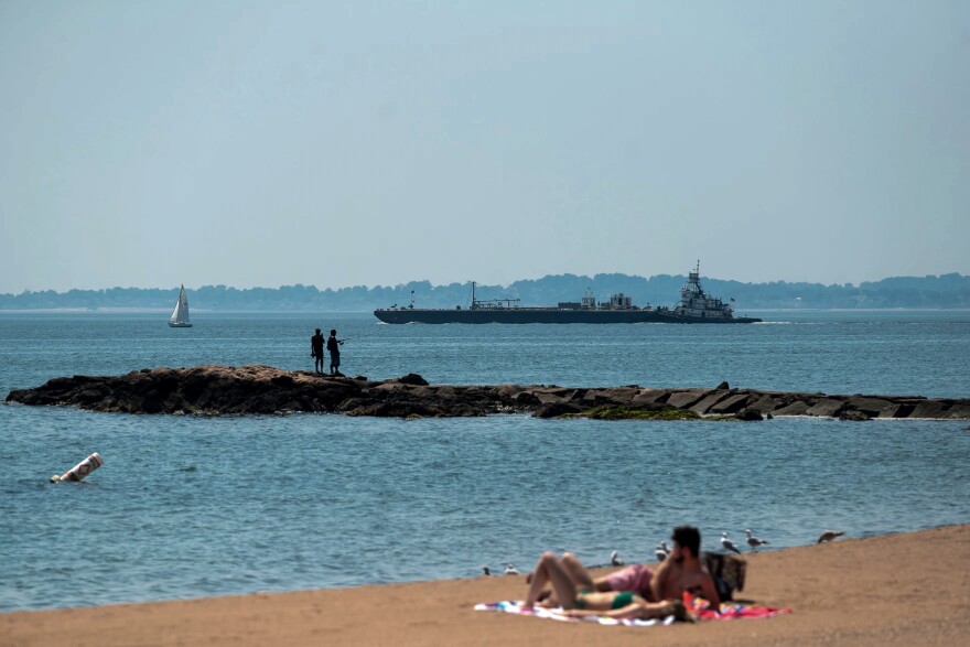 Beachgoers take refuge from the August heat by the waterside at Lighthouse Point Park as boats leave the nearby harbor in 2022.