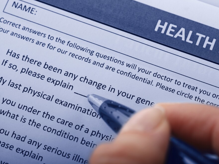 A hand holding a pen is about to fill out a health insurance form.