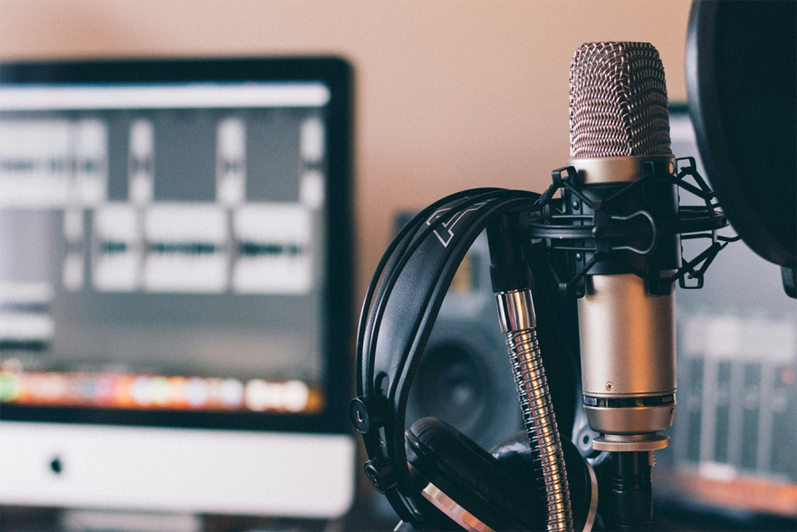 A grey microphone with headphones hung on it in front of a blurry background.