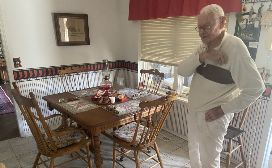 Bill Wantland standing next to a dining table and chairs set that belonged to his grandparents, the Lindsays