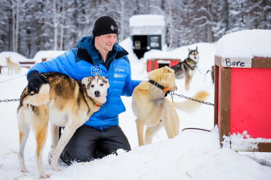 a person in a blue jacket petting his sled dogs