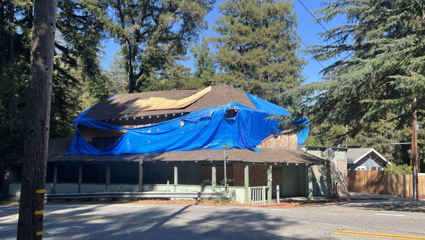 A dilapidated building is covered in a large blue tarp and its windows are all boarded up.