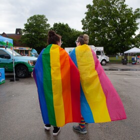  Two people wearing Pride flags walk around a Pride festival in New Hampshire in June, 2023.